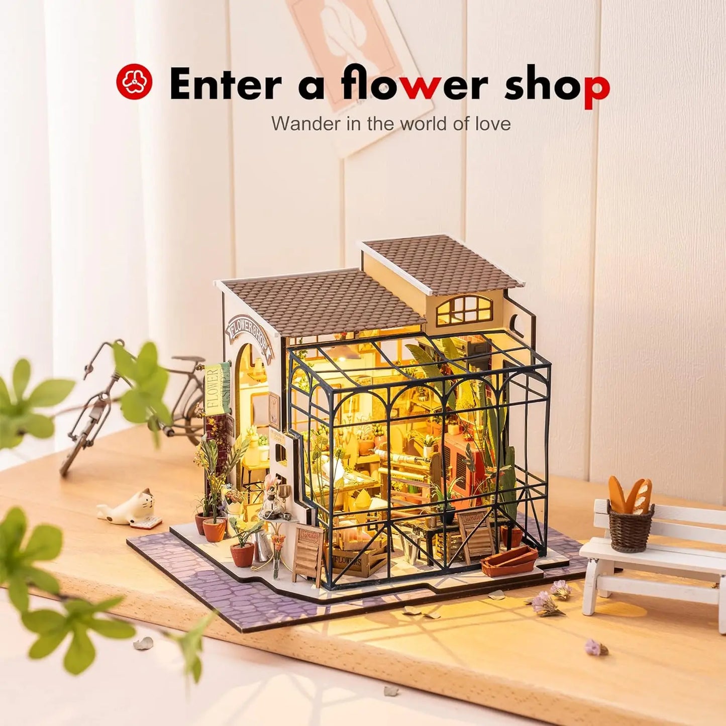 Miniature flower shop model with glass walls, plants, and warm lighting on wooden table