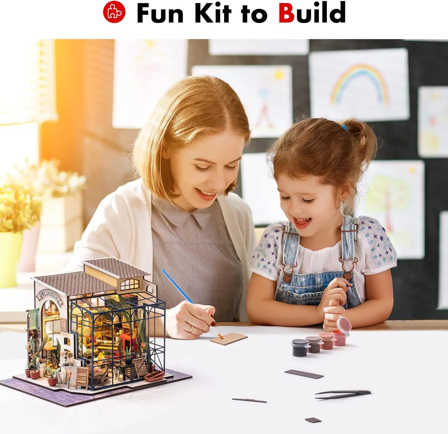 Mother and daughter building a miniature house kit at a table, craft paints and tools visible